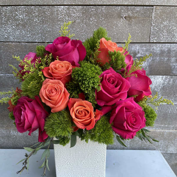 Pink and coral roses arranged in a white square vase