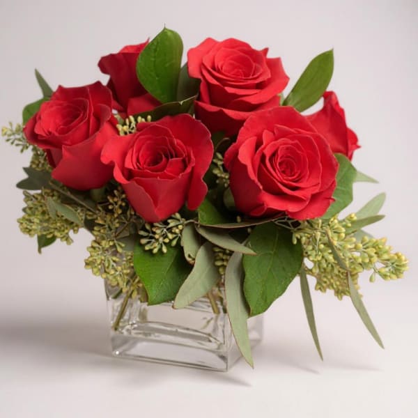 Red roses arranged in a clear square glass vase