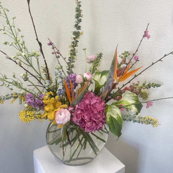 Mixed floral arrangement in a round glass vase with pink, yellow, purple, and orange blooms