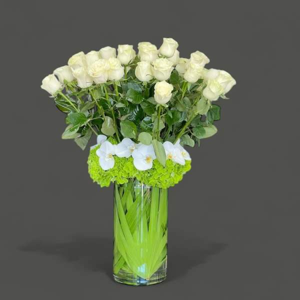 White roses and orchids in a tall clear vase with bright green flowers