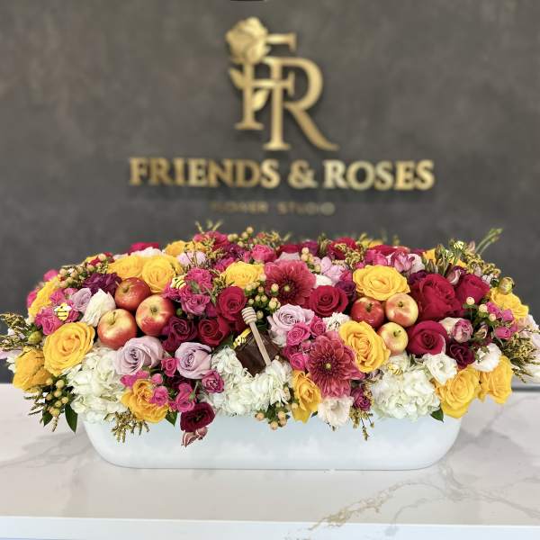 Large mixed flower arrangement in a white rectangular container with apples