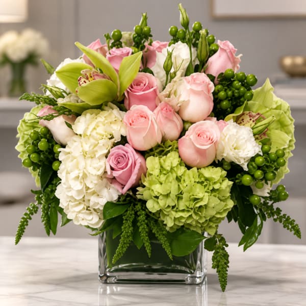Pink and white roses in a clear square vase with green hydrangea