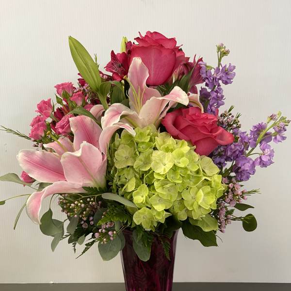 Pink lilies, roses, hydrangea, and purple flowers in a magenta vase