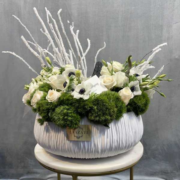 White floral arrangement in a large pleated vase with green accents