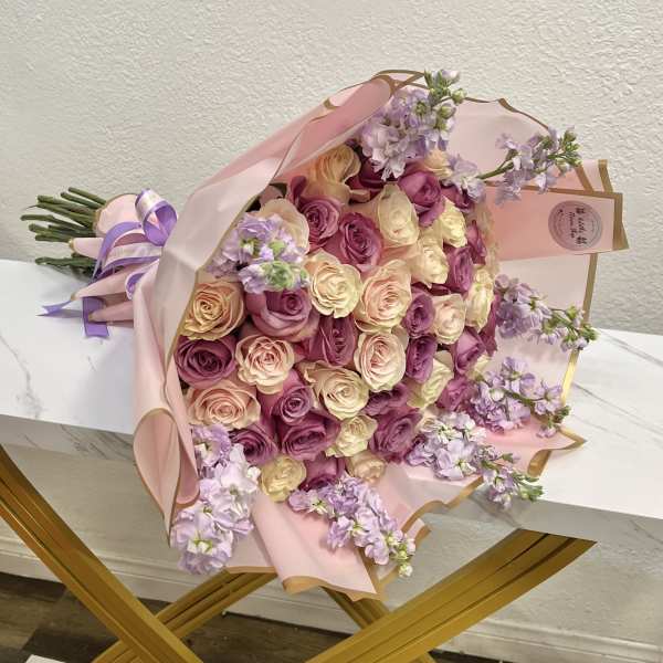 Bouquet of pink, cream, and lavender roses wrapped in pale pink paper