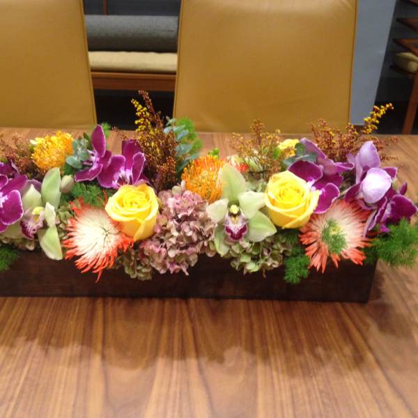 Long rectangular floral centerpiece with purple orchids and yellow roses