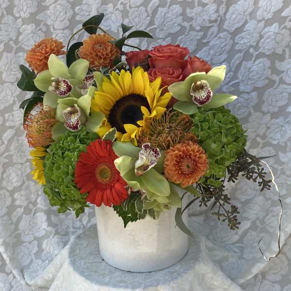Mixed bouquet with sunflowers, roses, orchids, and dahlias in a white vase