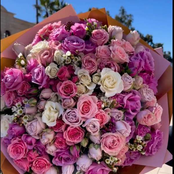 Large bouquet of pink, purple, and white roses wrapped in pastel paper