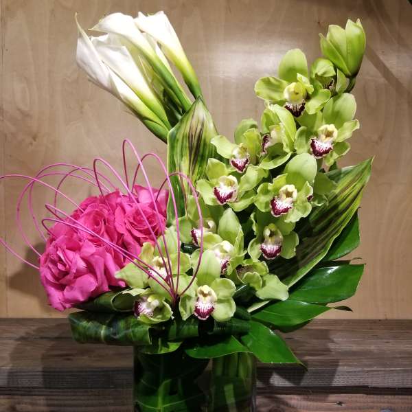 Pink roses and green orchids in a tall glass vase with white calla lilies