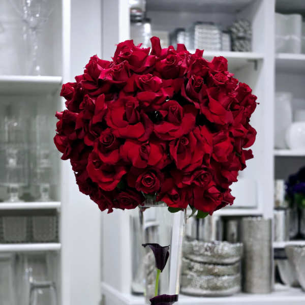 Tall bouquet of red roses in a clear vase with dark calla lilies