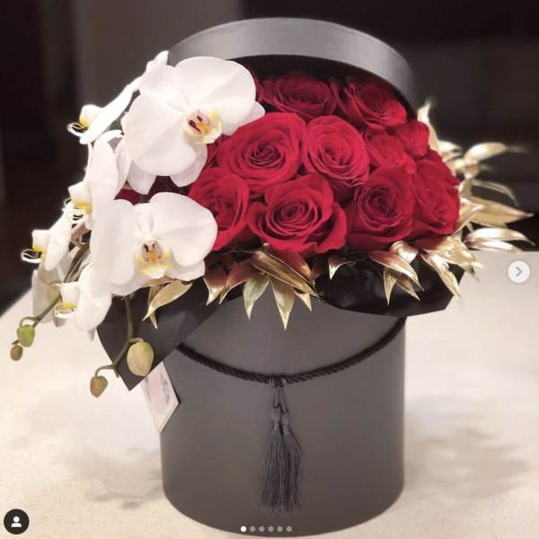 Red roses and white orchids arranged in a black hat box
