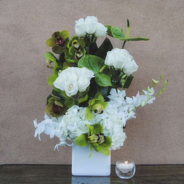 White floral arrangement in a square vase with a small candle beside it