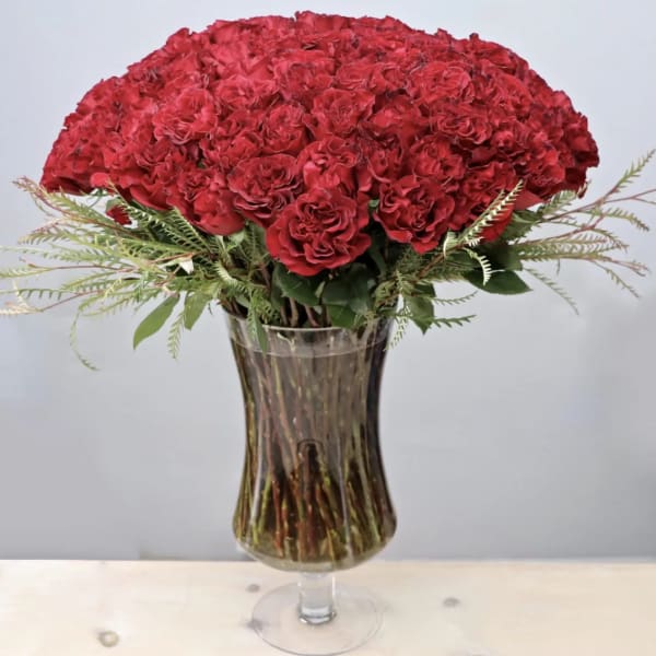Tall bouquet of red carnations with feathery accents in a clear pedestal glass vase