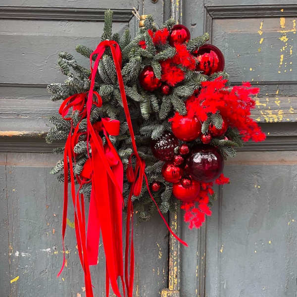 Holiday wreath with red ornaments and ribbon on a gray door