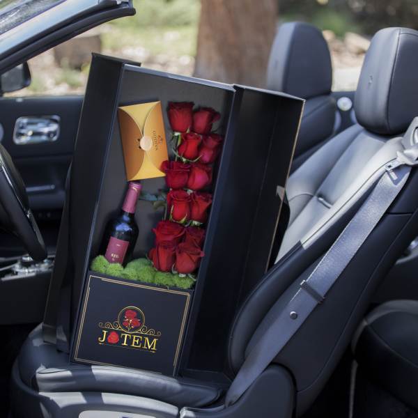 Boxed arrangement of red roses with a wine bottle and card in a car seat