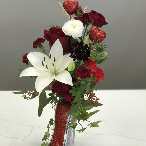 Red and white floral arrangement in a glittery high-heel vase with heart picks