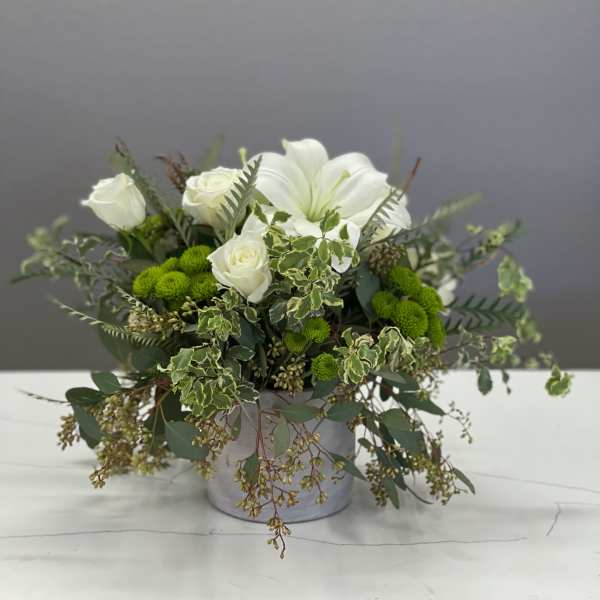 White roses and lilies in a gray container with trailing greenery