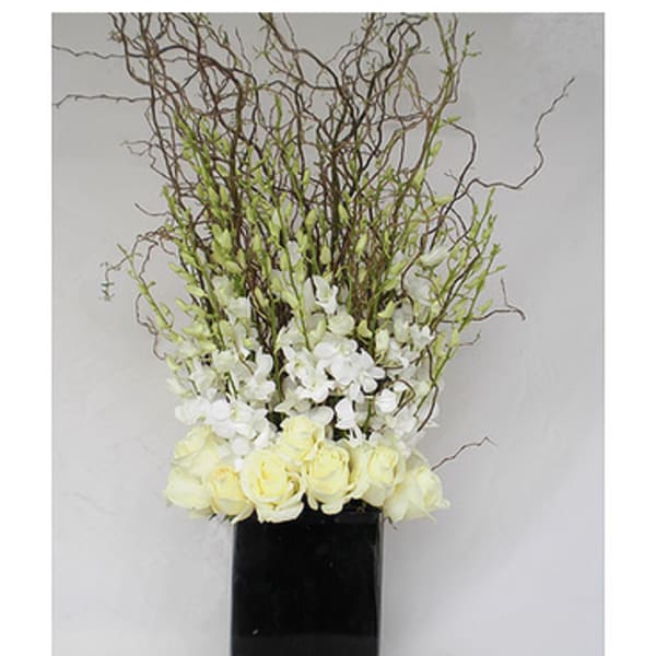 White roses and orchids in a tall black vase with curly branches