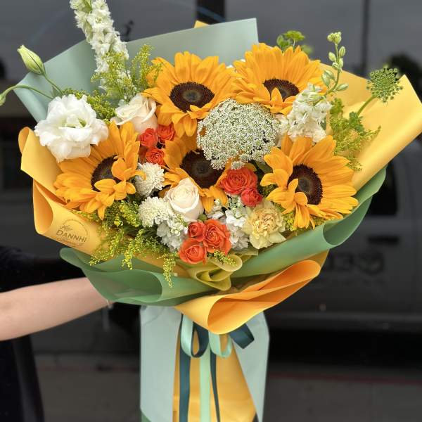 Bouquet of sunflowers, roses, and white blooms wrapped in yellow and green paper
