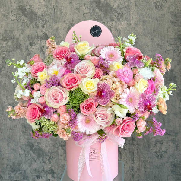 Large pink floral arrangement in a round pink box with a lace ribbon