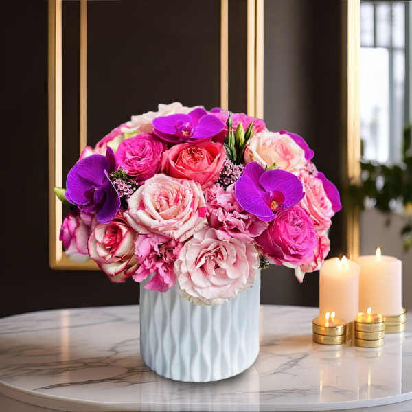 Pink and purple rose bouquet in a white vase beside candles