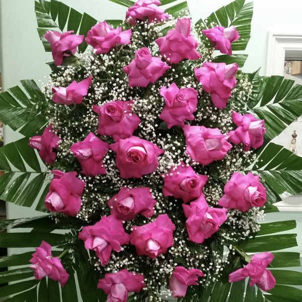 Tall standing spray of pink roses with baby's breath and palm leaves