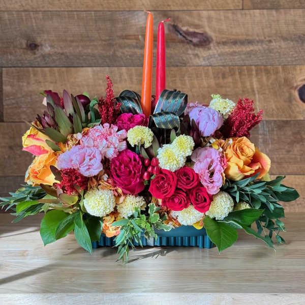 Colorful floral centerpiece with two taper candles in a low rectangular container