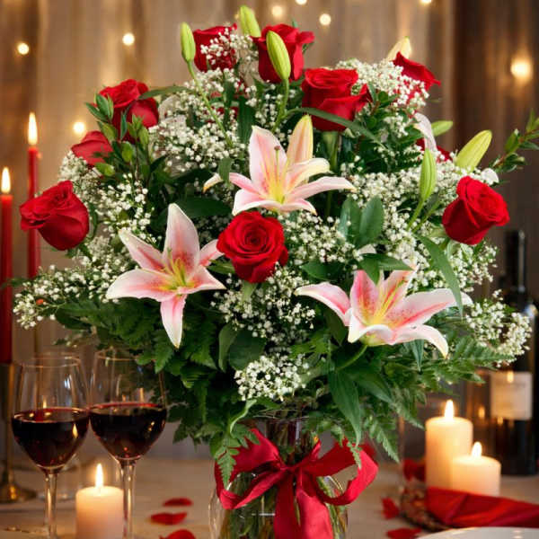 Bouquet of red roses and pink lilies in a glass vase with a red ribbon