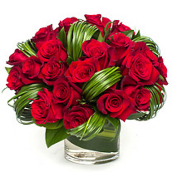 Red rose bouquet in a clear glass vase with folded green leaves