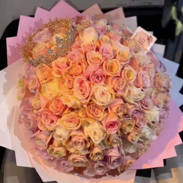 Large bouquet of pastel roses wrapped in pink paper with a decorative crown