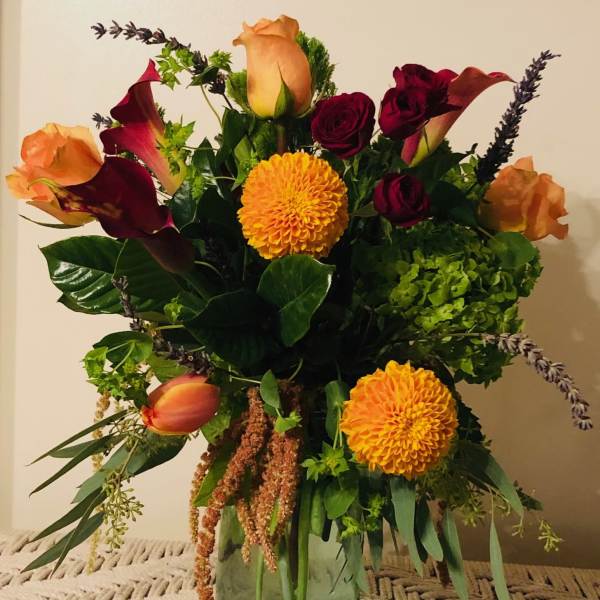 Mixed bouquet with orange roses, burgundy calla lilies, and yellow dahlias in a glass vase