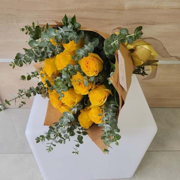 Wrapped bouquet of bright yellow roses and eucalyptus laid on a white stand