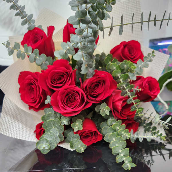 Hand-tied bouquet of red roses with eucalyptus accents wrapped in cream textured paper