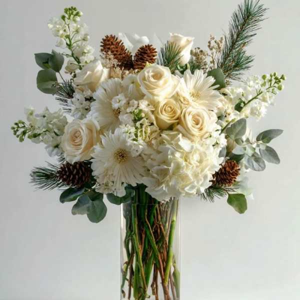 White roses and daisies arranged in a clear glass vase with pinecones and pine sprigs