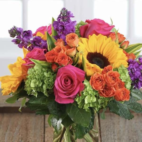 Mixed bouquet of roses, sunflowers, and purple blooms in a glass vase