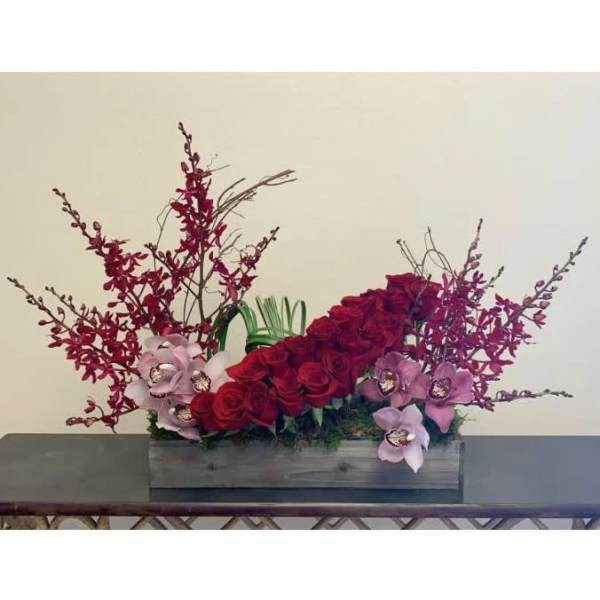 Red roses and pink orchids arranged in a rectangular wooden box