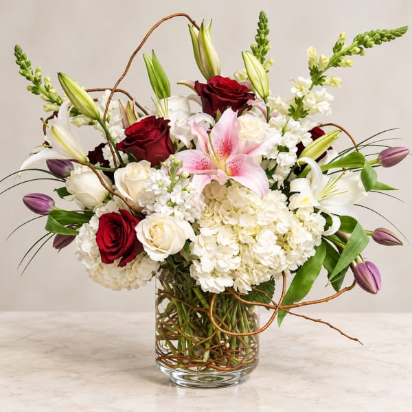 Bouquet of red and white roses, lilies, and hydrangeas in a glass vase