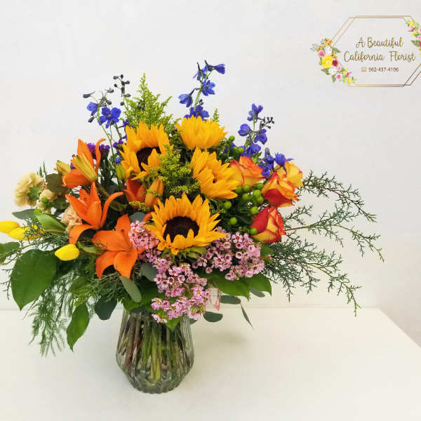 Mixed bouquet with sunflowers, lilies, roses, and blue flowers in a glass vase