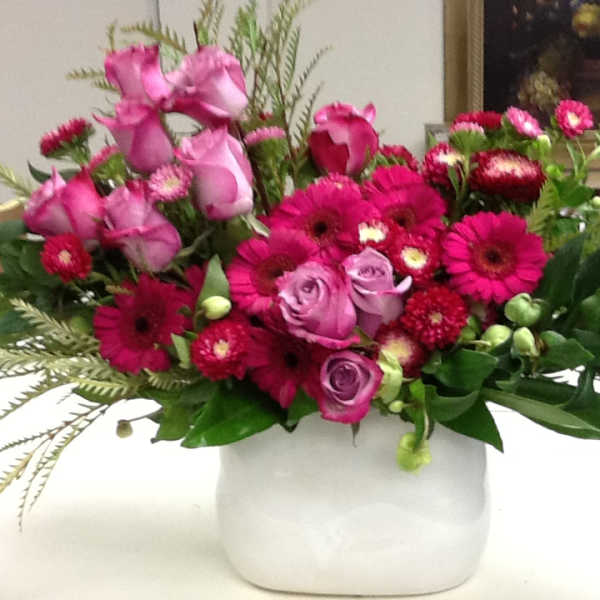 Pink roses and magenta daisies arranged in a white vase