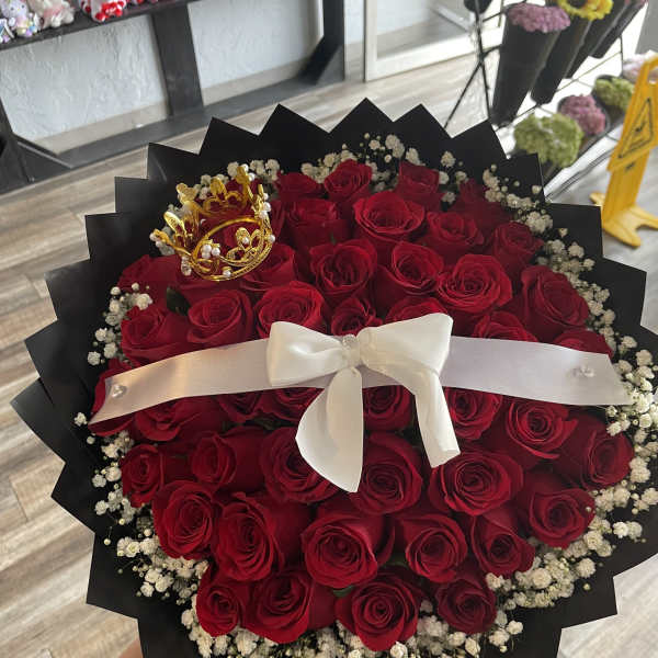 Bouquet of red roses with a white ribbon and gold crown topper