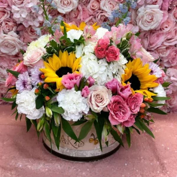Round floral arrangement with sunflowers, pink roses, and white blooms in a decorative box