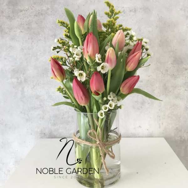 Pink tulips arranged in a clear glass vase with small white filler flowers