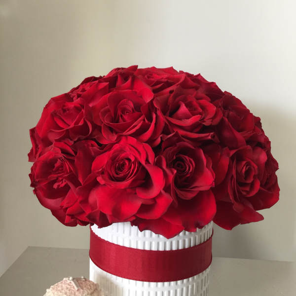 Red rose bouquet in a white textured vase with a red ribbon