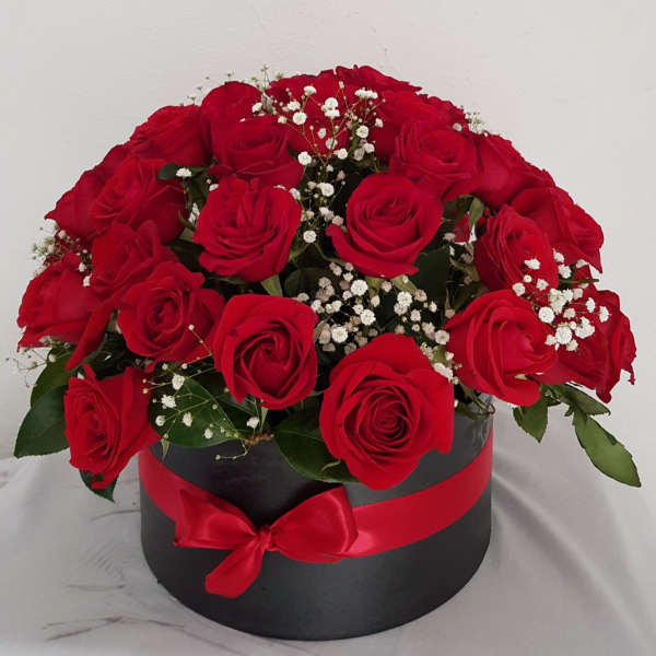 Red roses arranged in a black round box with a red ribbon