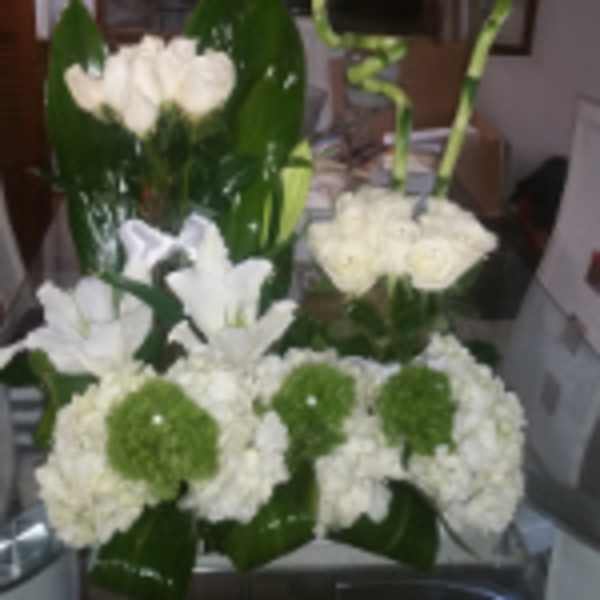 Modern arrangement of white roses, lilies, and hydrangeas with green accents in a low glass container