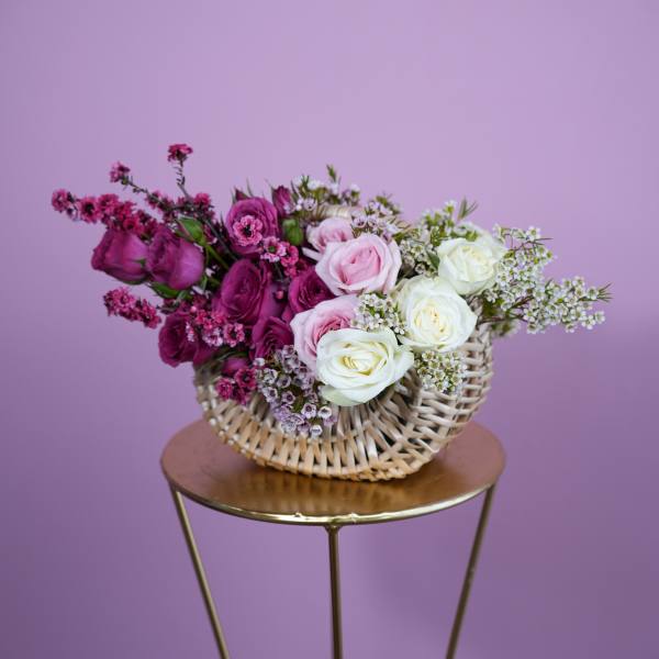 Pink and white roses in a woven basket on a small stand