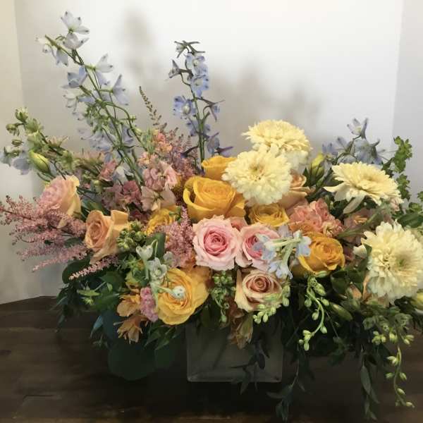 Mixed bouquet of roses, dahlias, and blue delphinium in a low container