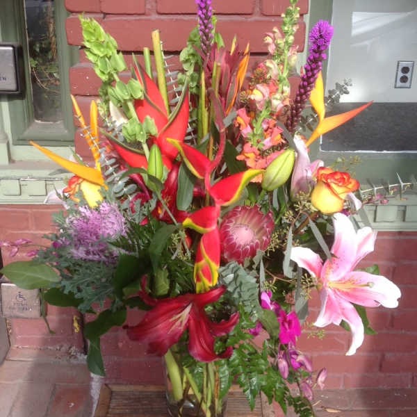 Tall tropical bouquet with lilies, calla lilies, and protea in a glass vase