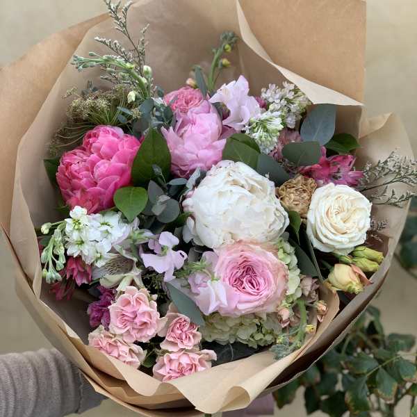 Hand-tied bouquet of pink and white flowers wrapped in brown paper