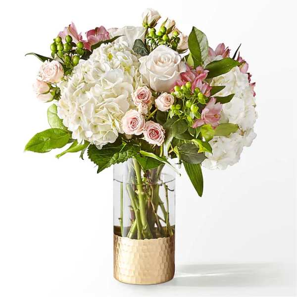 White hydrangeas and pale pink roses in a clear glass vase with a gold base